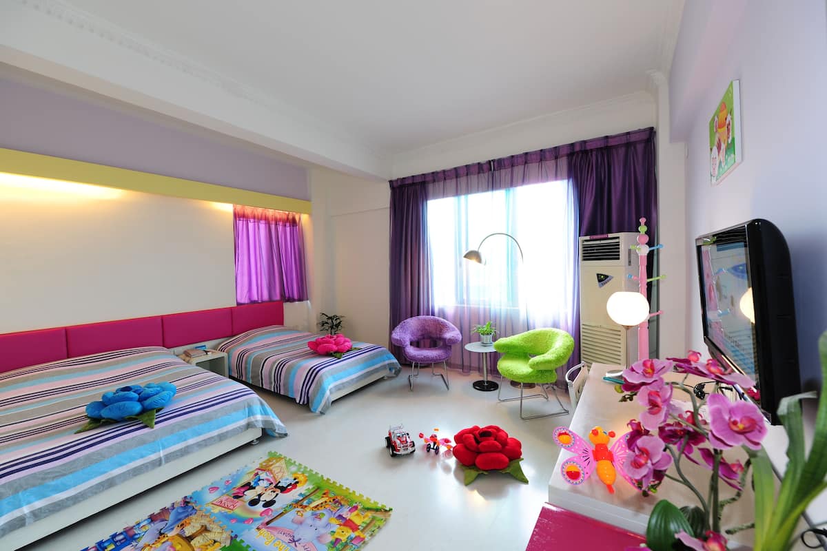 A bedroom with two beds, a chair, a TV, and a window with curtains.