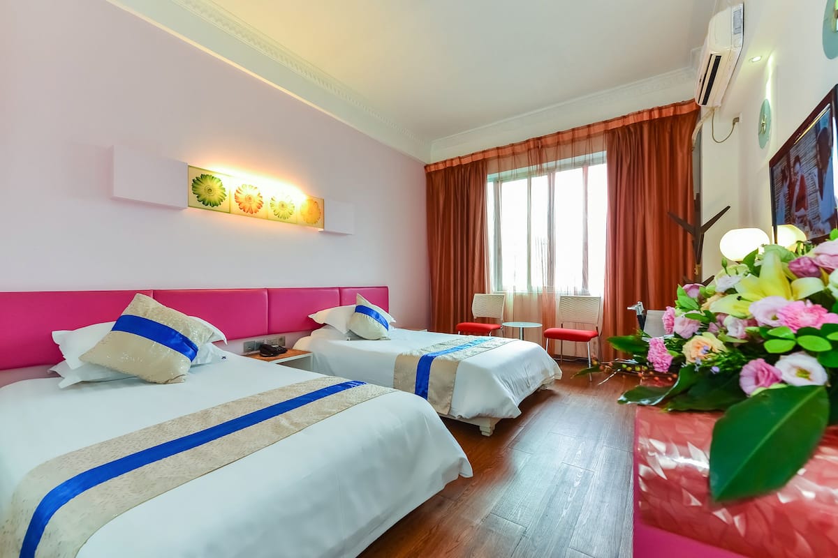 A hotel room with two beds, a red chair, a small table, and a large window with curtains.