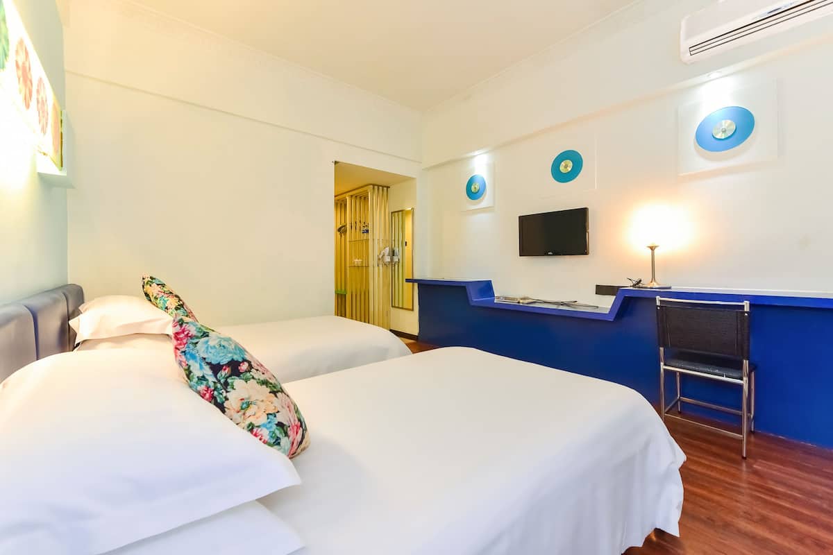 A hotel room with two beds, a desk, a chair, and a TV.