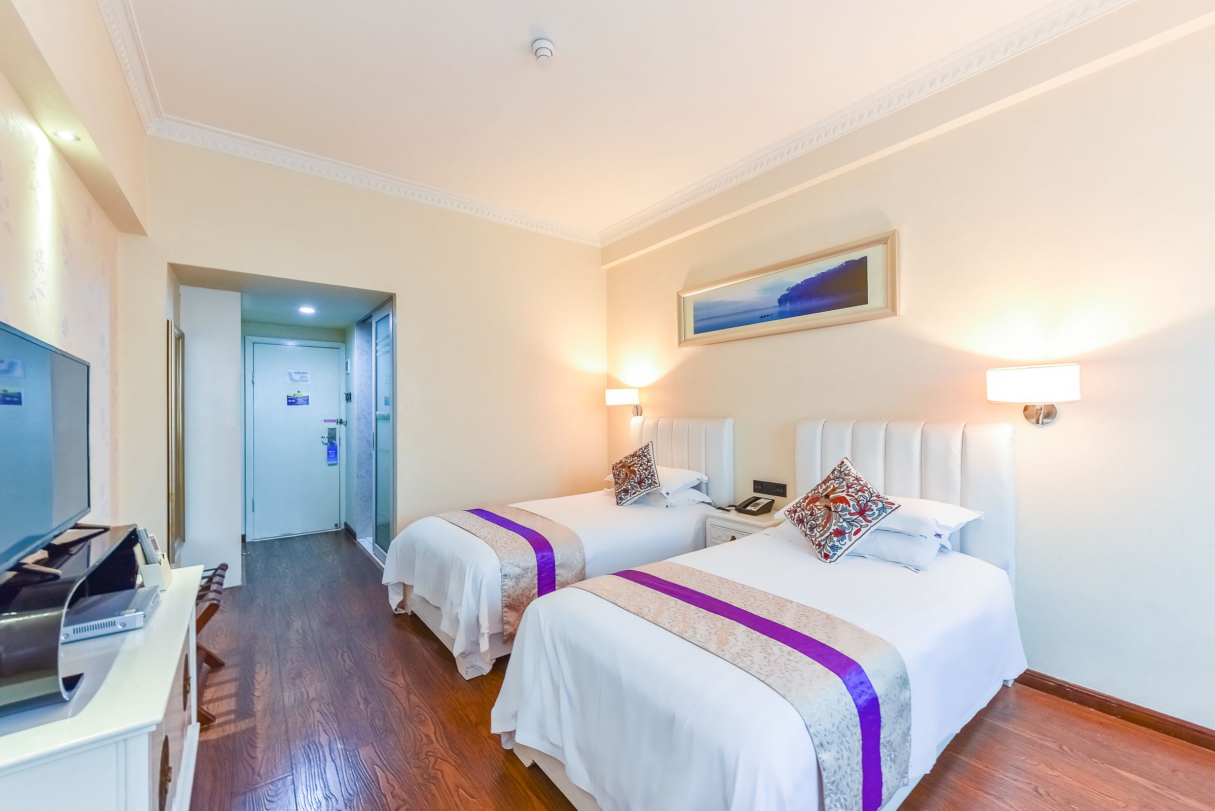 A hotel room with two beds, a TV, and a desk with a computer.