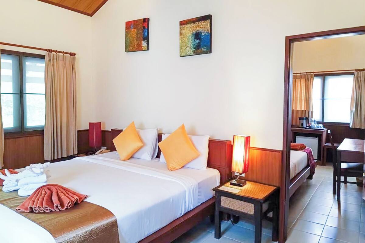 A hotel room with a bed, a bedside table with a lamp, a chair, a desk, and two paintings on the wall.
