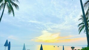 A beach with lounge chairs and umbrellas, palm trees, and a calm sea at sunset. - Pinnacle Samui Resort SHA Plus (Koh Samui)