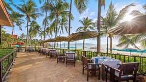 A beachside restaurant with outdoor seating, palm trees, and a view of the ocean. - Pinnacle Samui Resort SHA Plus (Koh Samui)