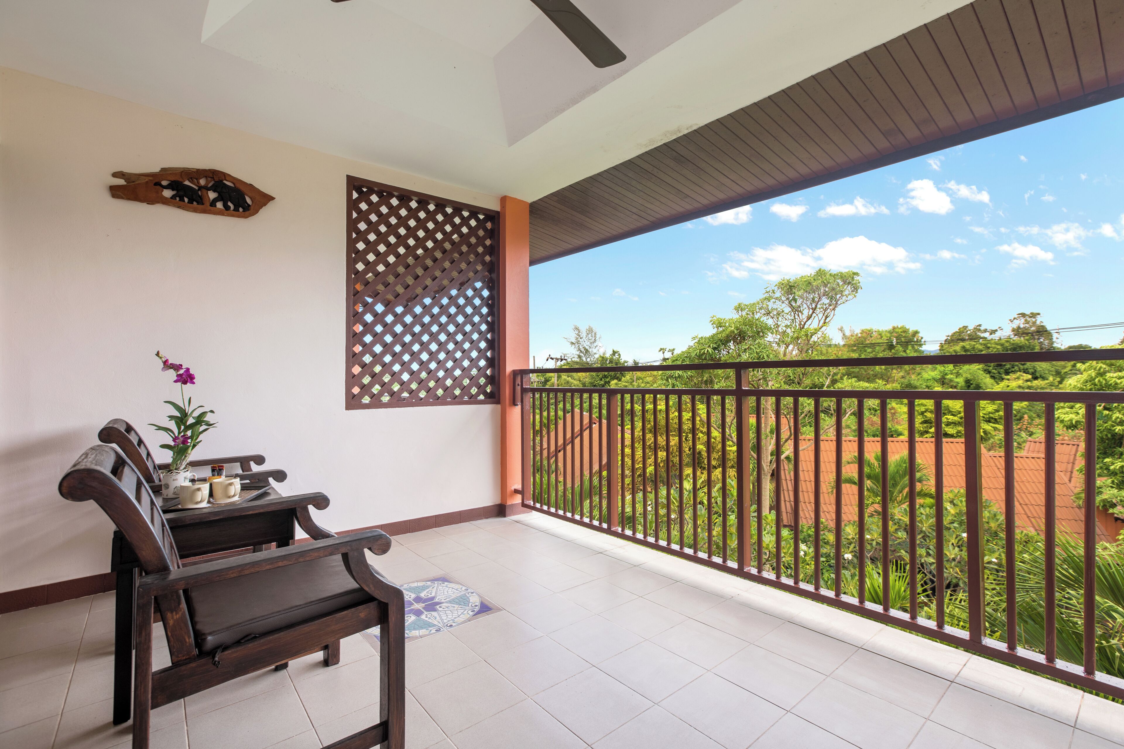 A balcony with a wooden bench, a small table with a flower, and a decorative wall panel.