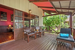 A wooden deck with seating, a view of lush greenery, and a red wall with artwork.