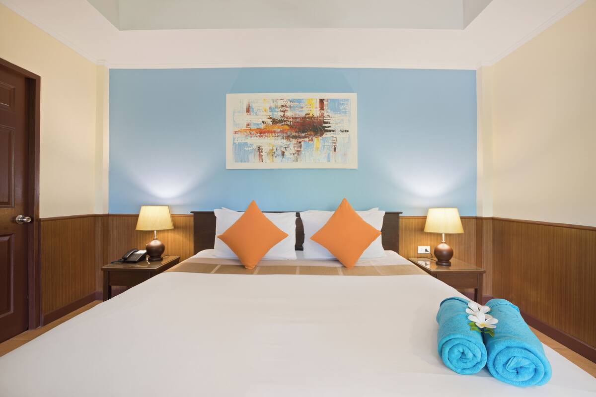 A hotel room with a large bed, two nightstands, a painting on the wall, and a blue towel on the bed.