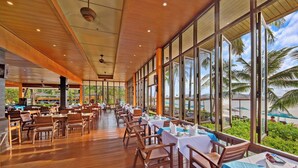 A spacious indoor dining area with wooden flooring and large windows offering views of palm trees and a beach. - Pinnacle Samui Resort SHA Plus (Koh Samui)