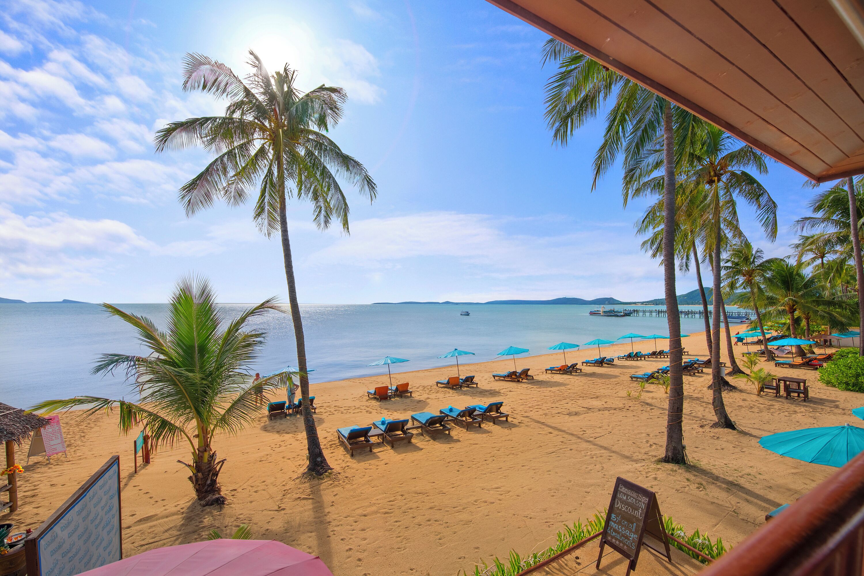 A beach with palm trees, lounge chairs, and umbrellas.