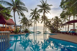 A pool area with palm trees, lounge chairs, and a building with a red roof. - Pinnacle Samui Resort SHA Plus (Koh Samui)