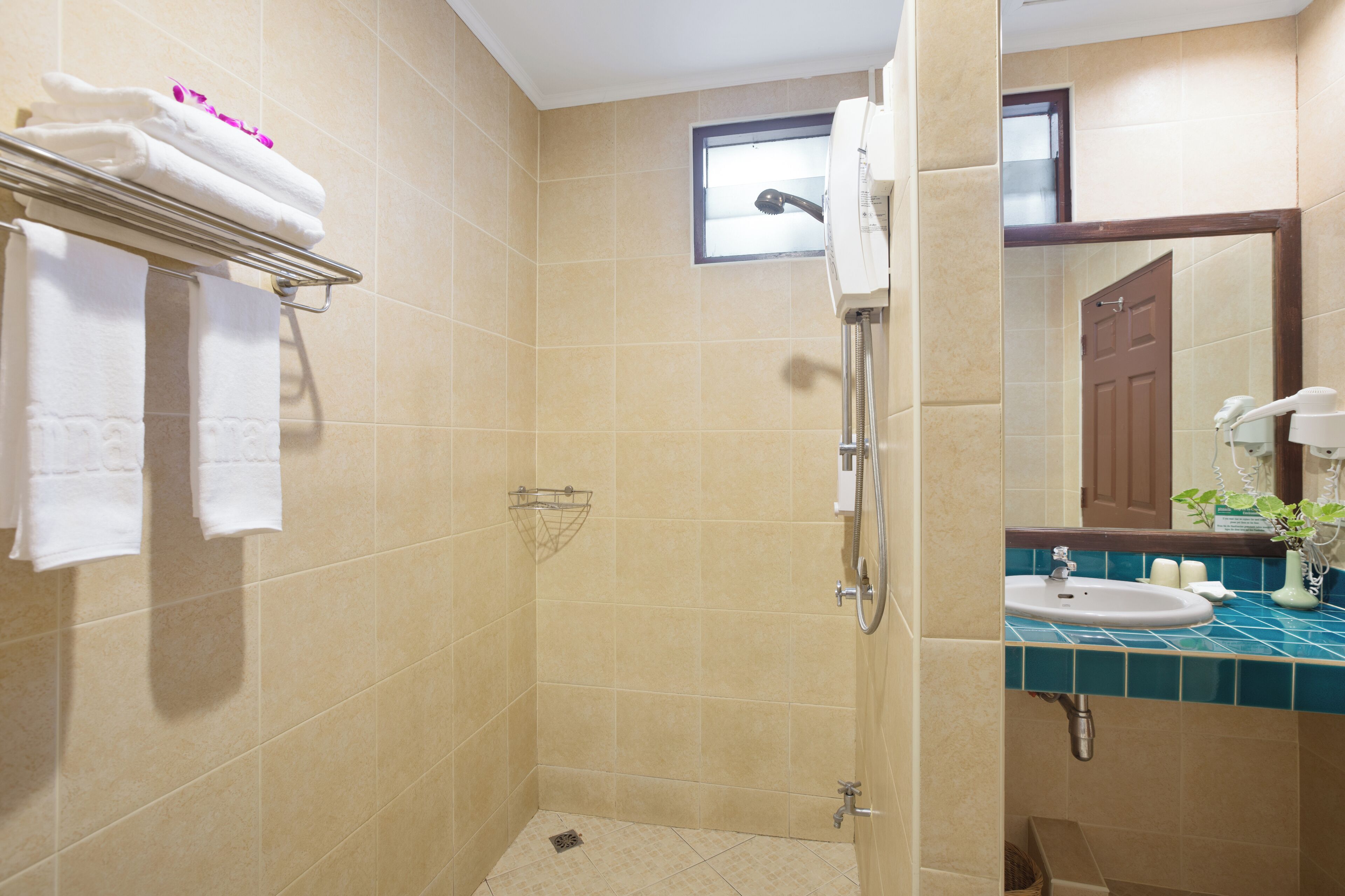 A bathroom with beige tiles, a shower, a sink with a blue countertop, and a towel rack with folded towels.