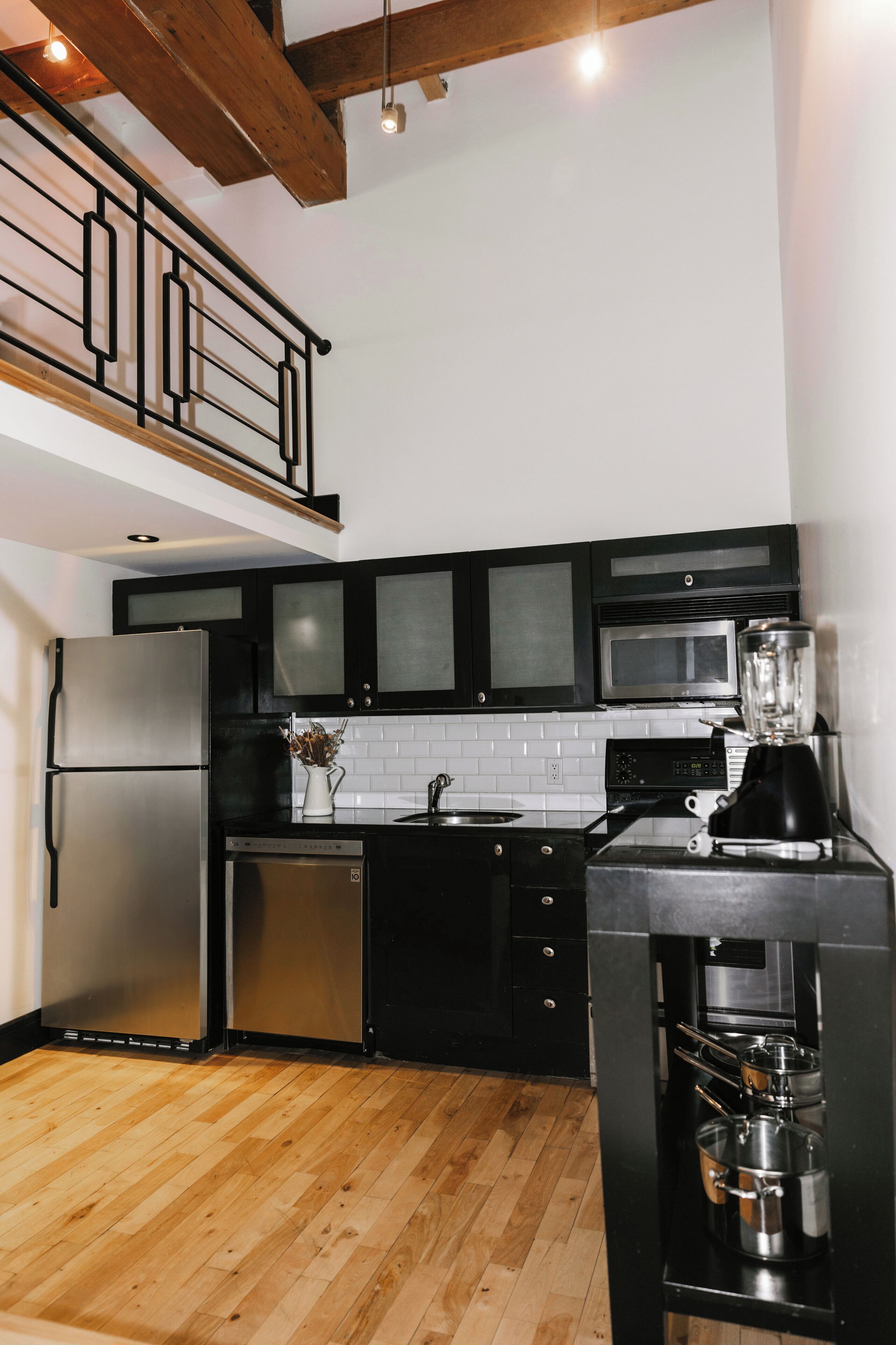 A modern kitchen with black cabinets, stainless steel appliances, and a wooden floor.