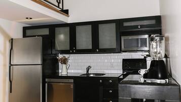 A modern kitchen with black cabinets, stainless steel appliances, and a wooden floor.