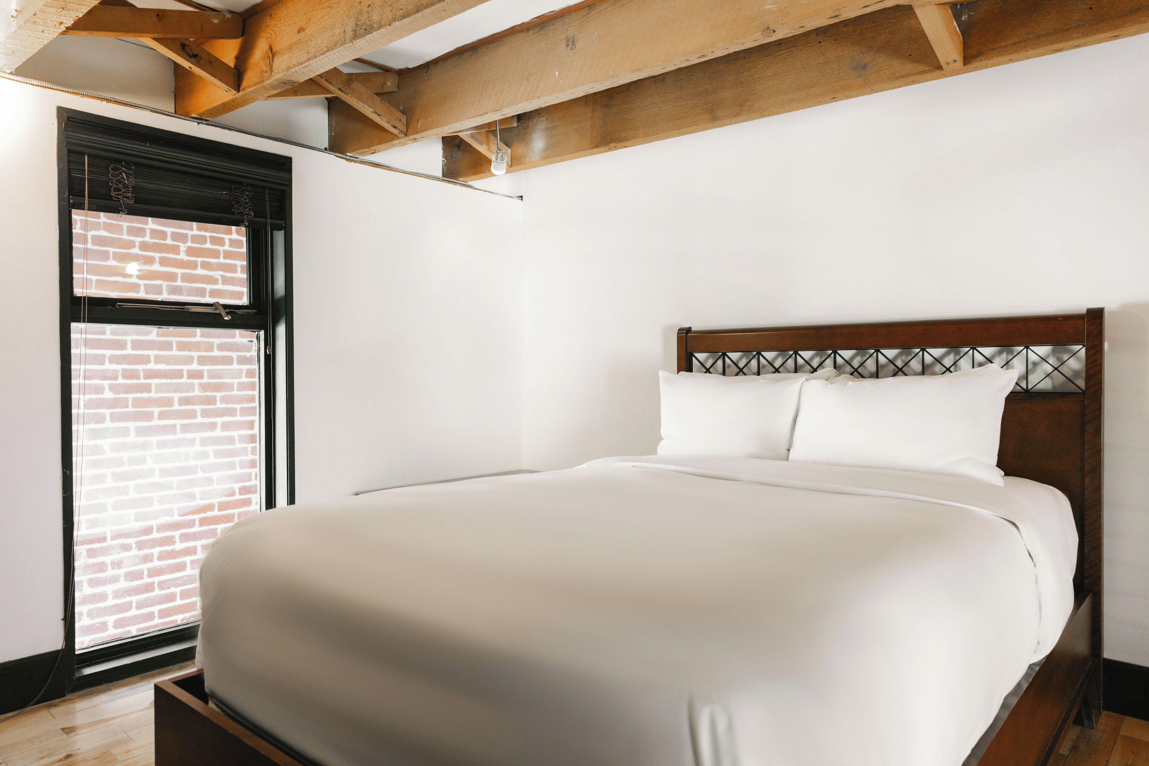Quarto com cama grande, vigas de madeira no teto, parede de tijolos e janela com persianas.