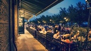 An outdoor dining area with tables and chairs, a covered walkway, and a stone building facade. - Lofts du Vieux-Port (Montreal)