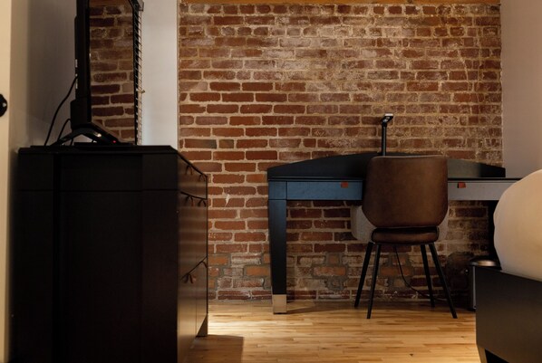 A room with a brick wall, a wooden floor, a desk, a chair, and a black cabinet.