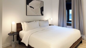 A neatly made bed with white linens, a modern bedside table with a lamp, and a large abstract painting above the bed.