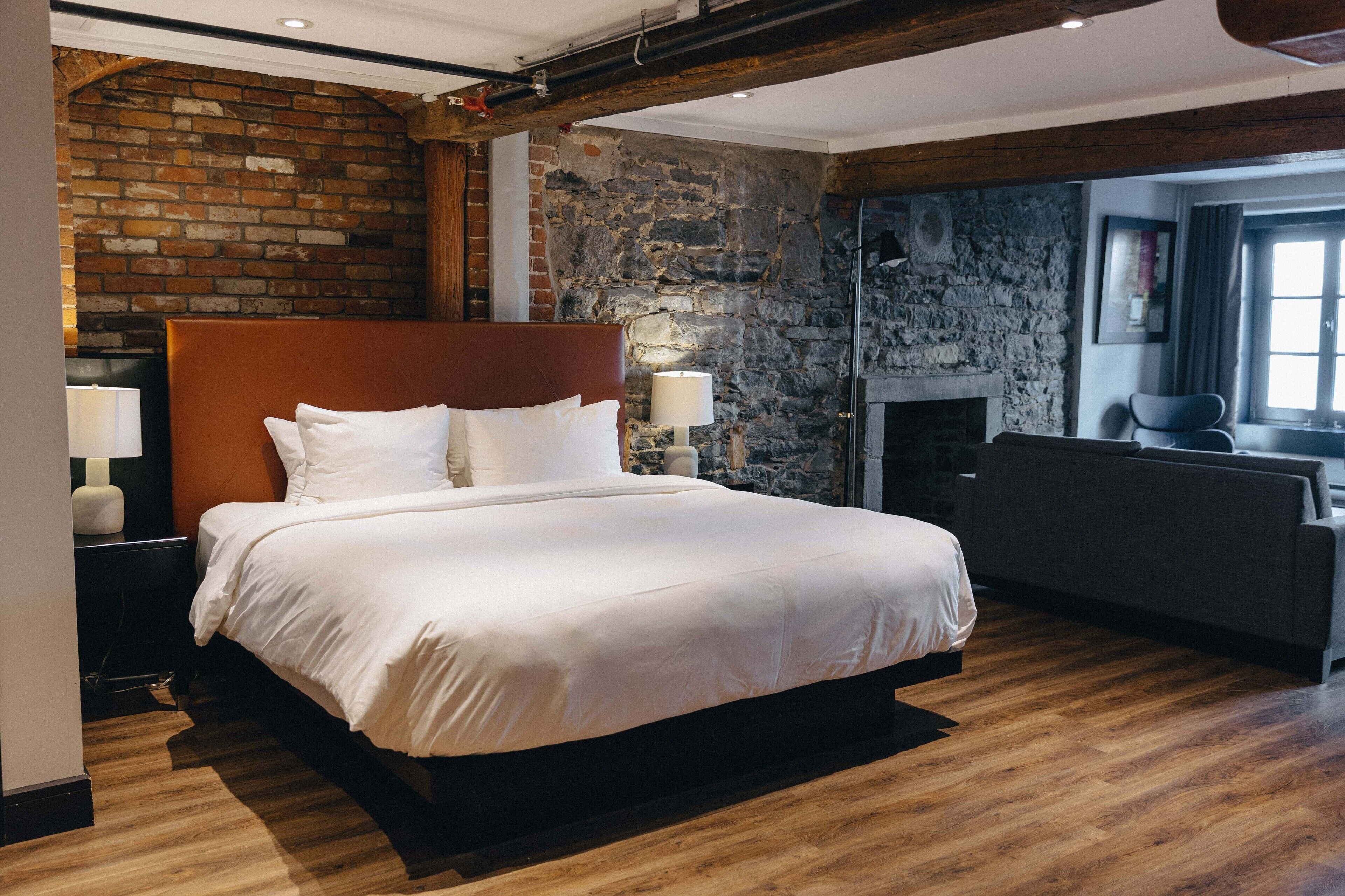 A modern hotel room with a large bed, a stone wall, and a fireplace.
