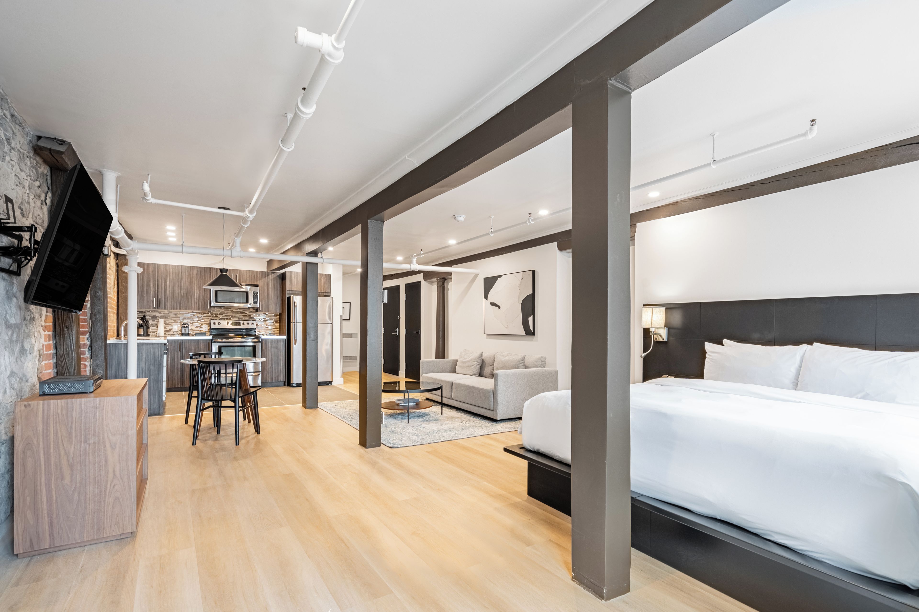 Una habitación de hotel moderna con una cama grande, un comedor con mesa y sillas, una cocina y una sala de estar con sofá.
