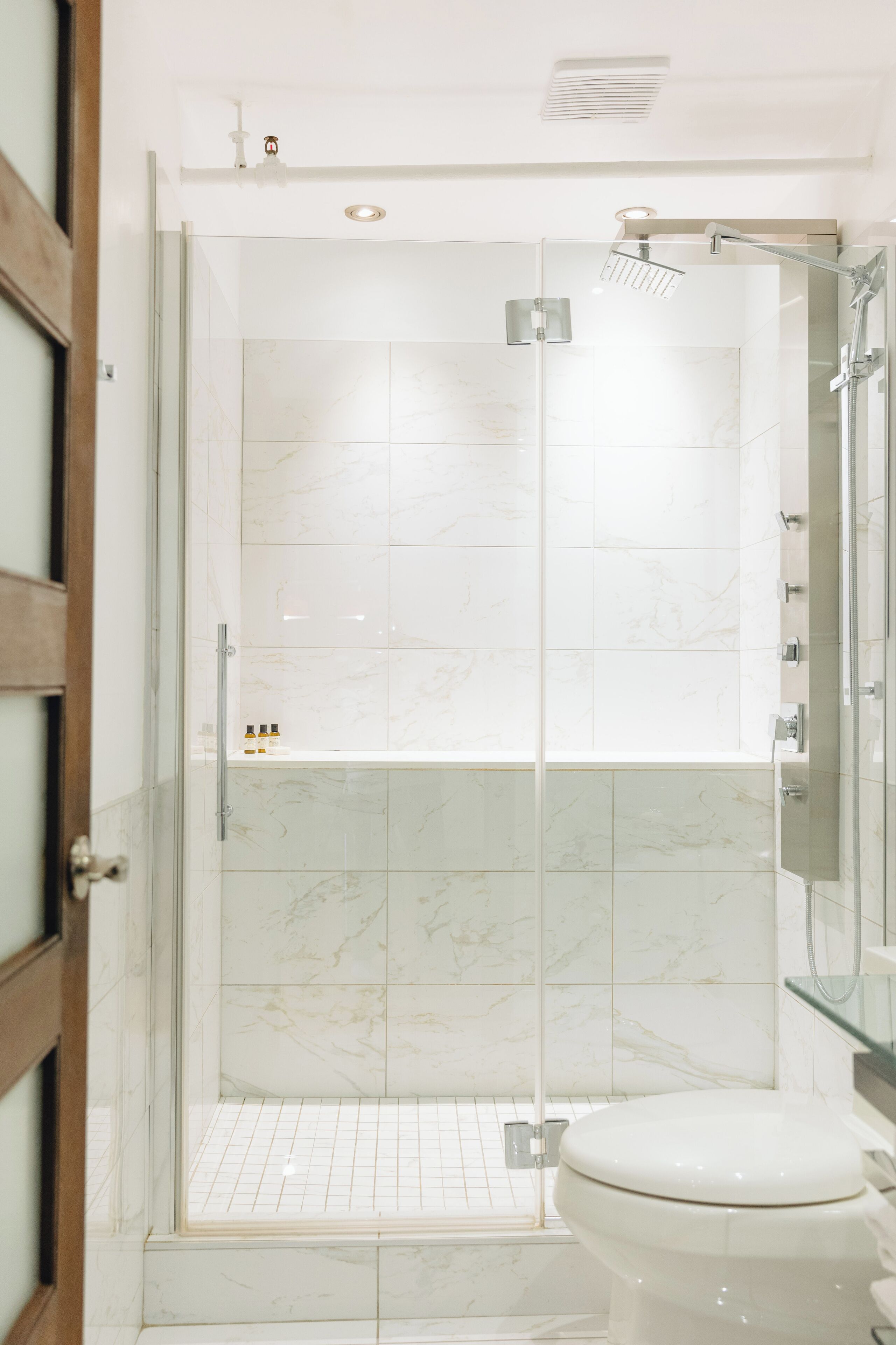 Ein modernes Badezimmer mit einer Glaskabine zur Dusche, einer Toilette und einer Wand mit Marmorfliesen.