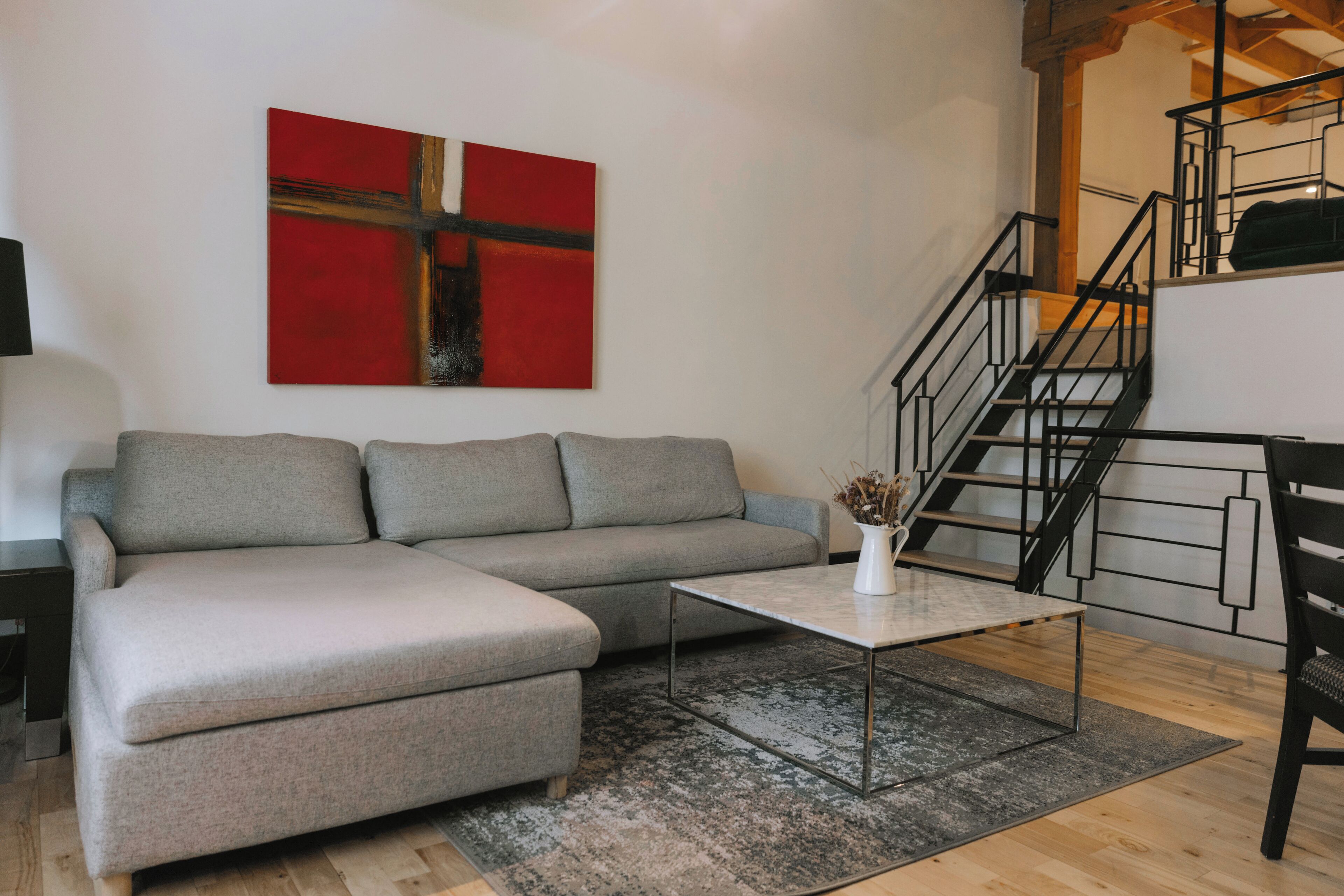 Een moderne woonkamer met een grijze modulaire bank, een klein bijzettafeltje en een abstract schilderij in rood op de muur.
