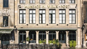 A historic building with the sign "Auberge du Vieux-Port" indicating a hotel. It features a classic facade with multiple windows and a covered entrance area with seating. - Lofts du Vieux-Port (Montreal)