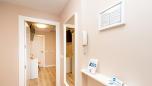 A hallway with a wooden floor, a white door, and a mirror on the wall. There is a shelf with a no smoking sign and a framed notice. - Gestión de Alojamientos Rooms - Guest House (Pamplona)