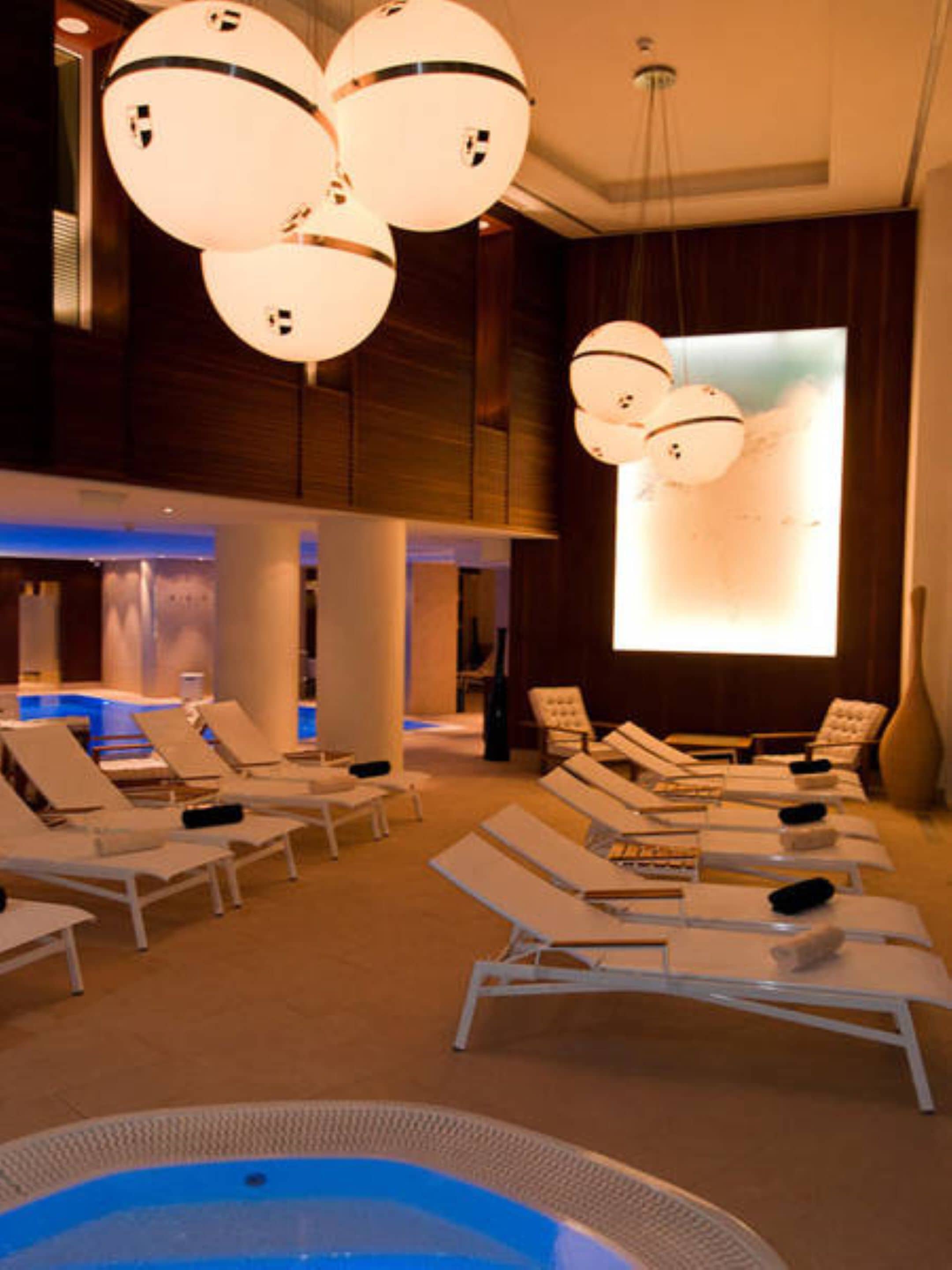 A spa area with lounge chairs, a hot tub, and a large screen displaying a beach scene.