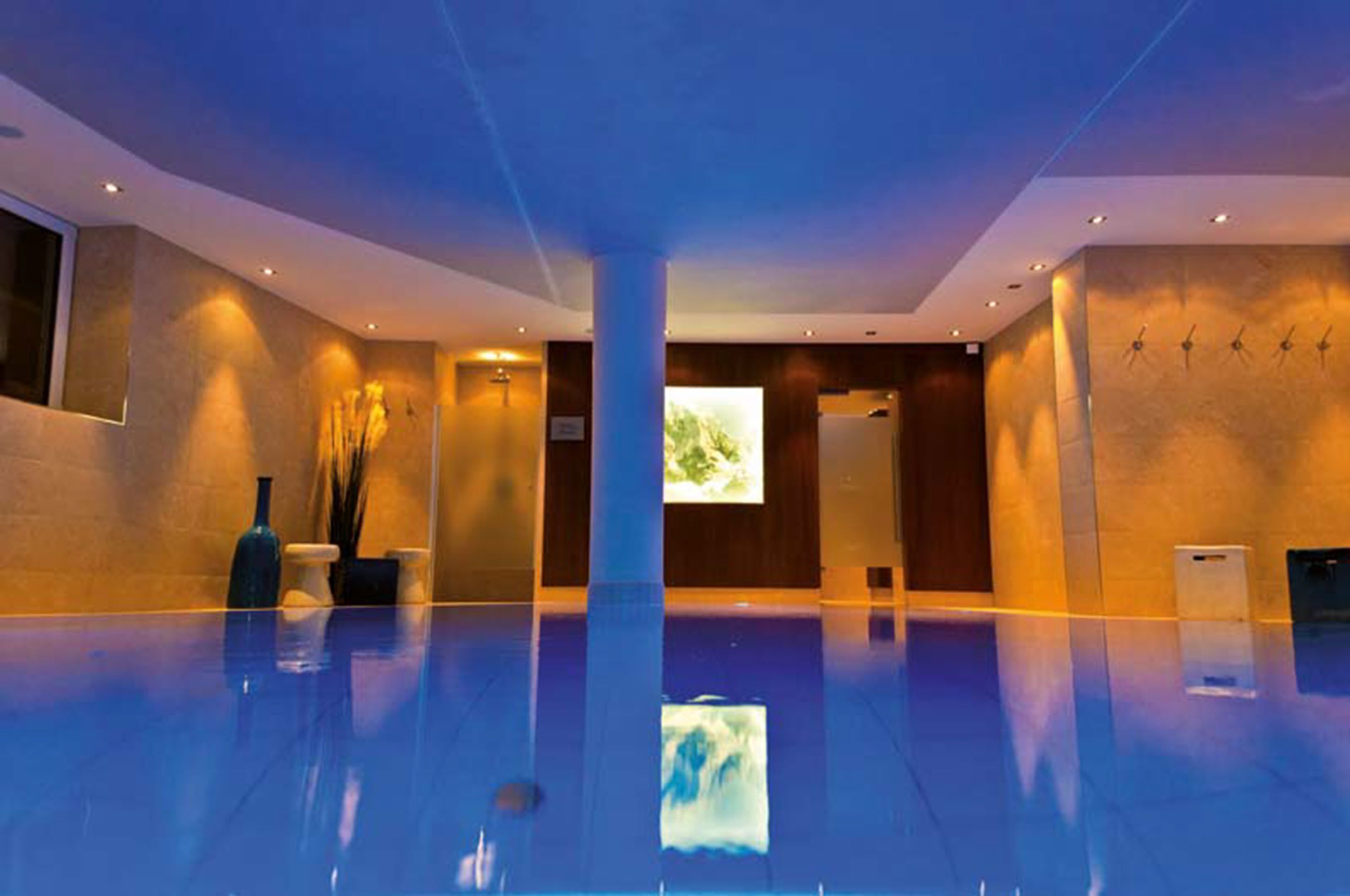 Un área de piscina interior espaciosa con una gran columna central, una pantalla de proyección en la pared y un diseño moderno con iluminación empotrada.