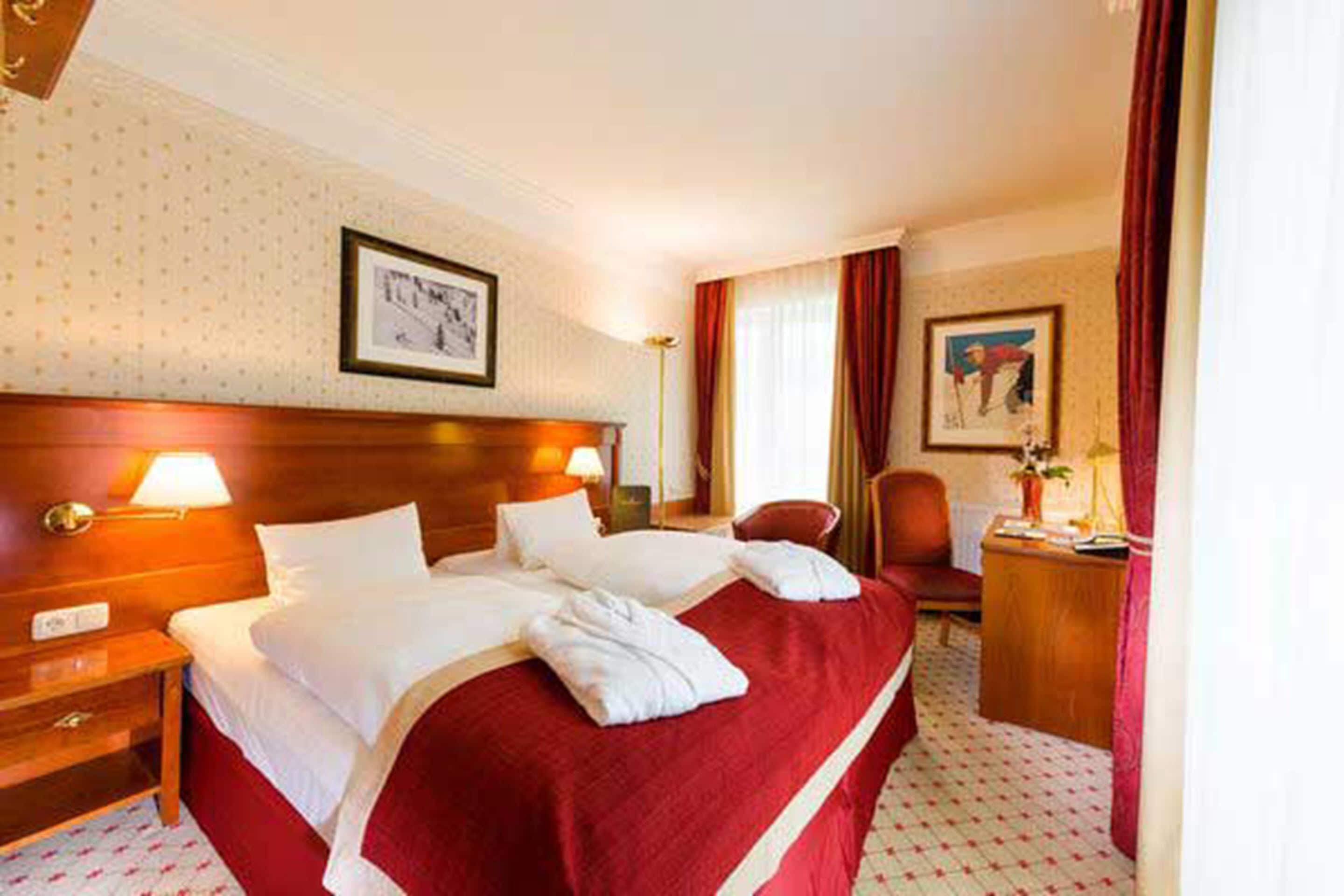 Een hotelkamer met een groot bed, een houten hoofdeinde, een nachtkastje, een bureau en een stoel.