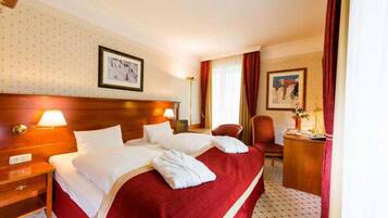 A hotel room with a large bed, a wooden headboard, a nightstand, a desk, and a chair.
