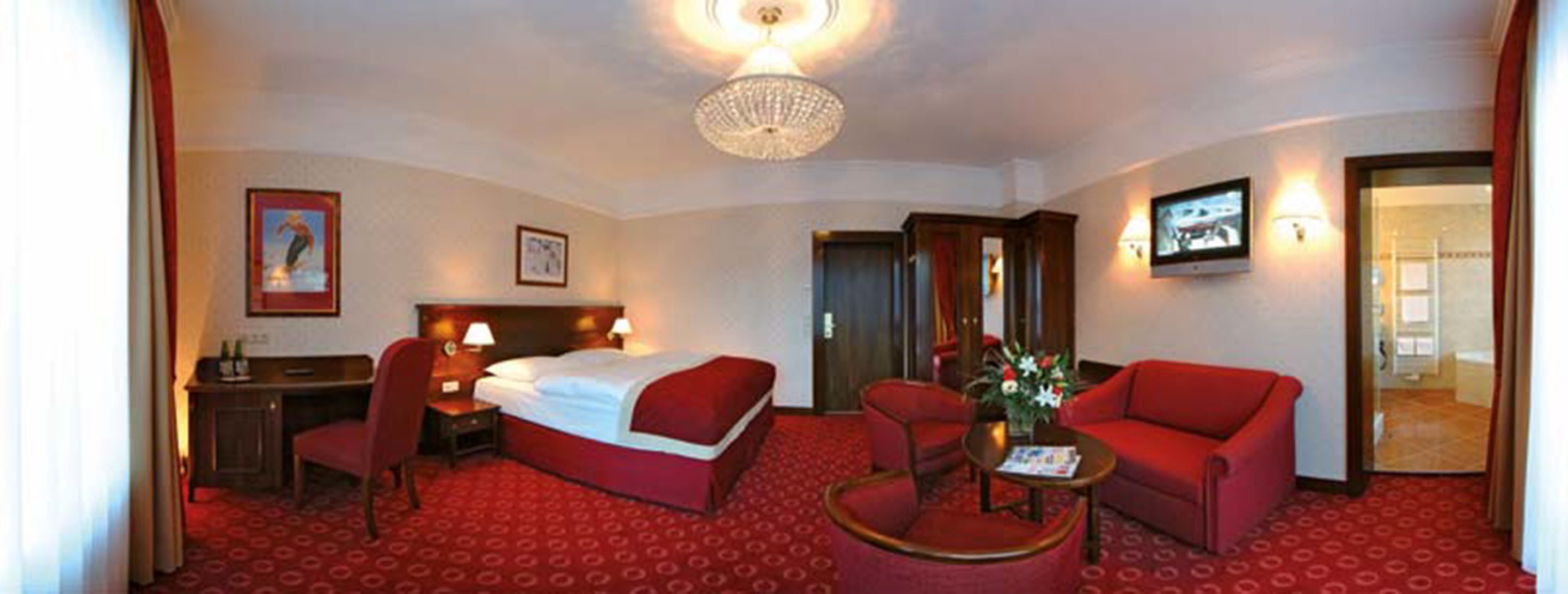 A hotel room with a bed, a desk, a chair, a sofa, and a small table with a vase of flowers.