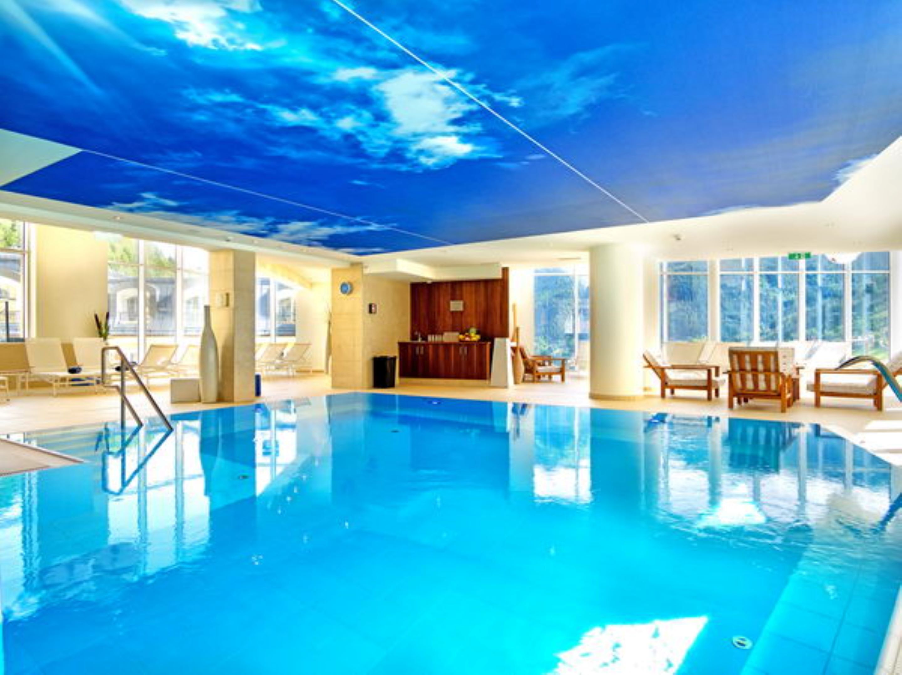 A large indoor swimming pool with clear blue water, surrounded by lounge chairs and a wooden cabinet.