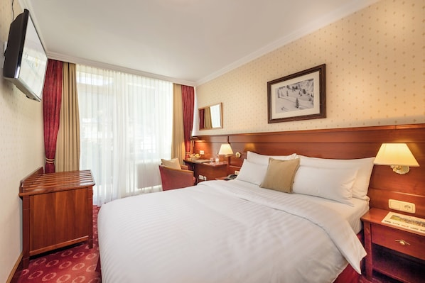 A hotel room with a large bed, a wooden nightstand, a desk, a chair, a TV, and a framed picture on the wall. - Hotel Salzburger Hof (Bad Gastein)