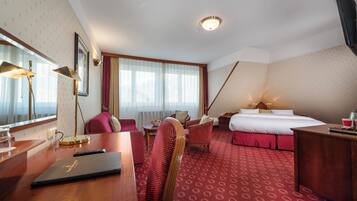 Habitación de hotel con cama, escritorio, silla, lámpara de escritorio, televisor y ventana con cortinas.