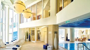 A spacious indoor swimming pool area with lounge chairs and a glass ceiling. - Hotel Salzburger Hof (Bad Gastein)