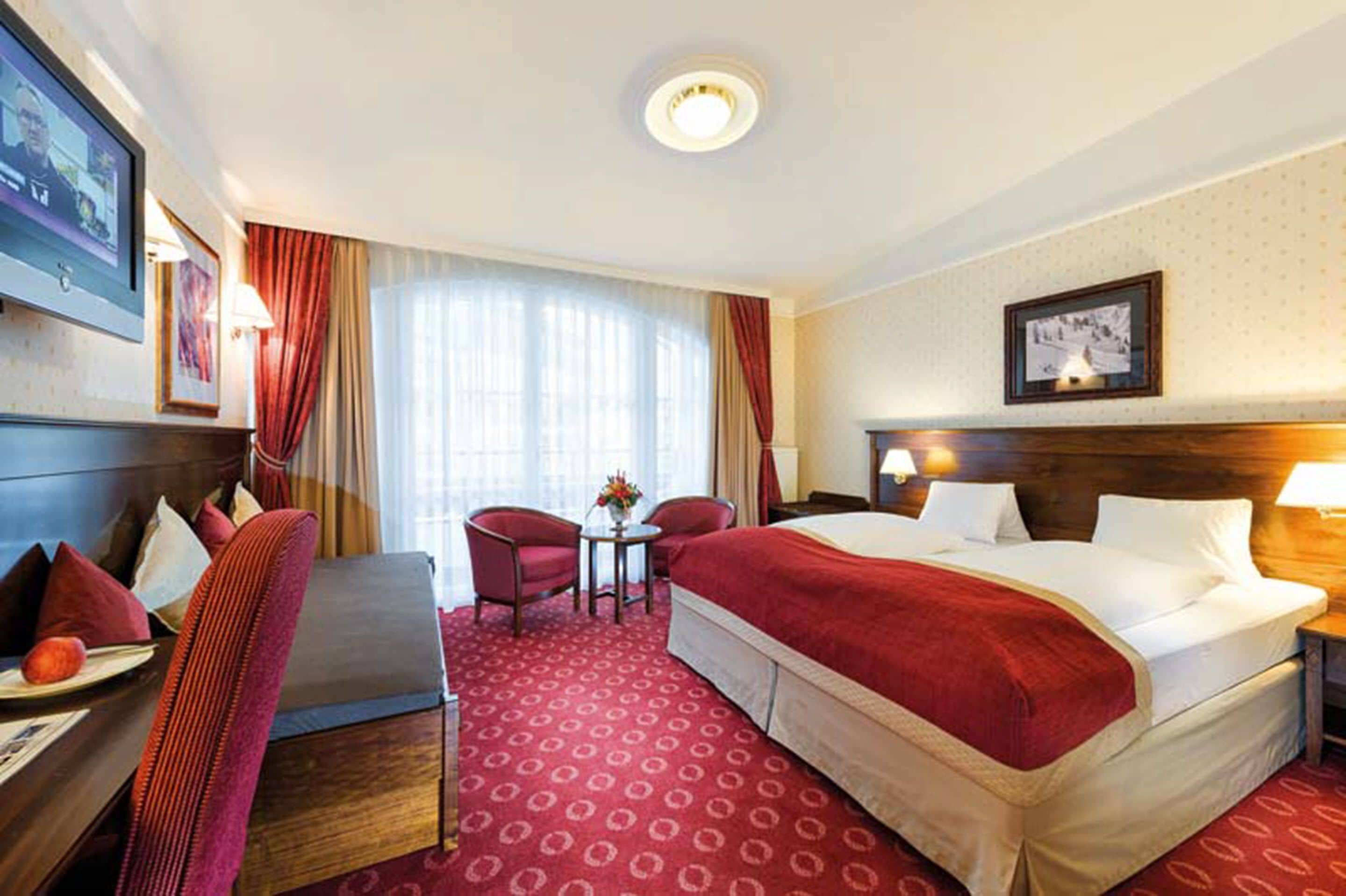 A hotel room with a large bed, a desk, a chair, and a small table with a vase of flowers.