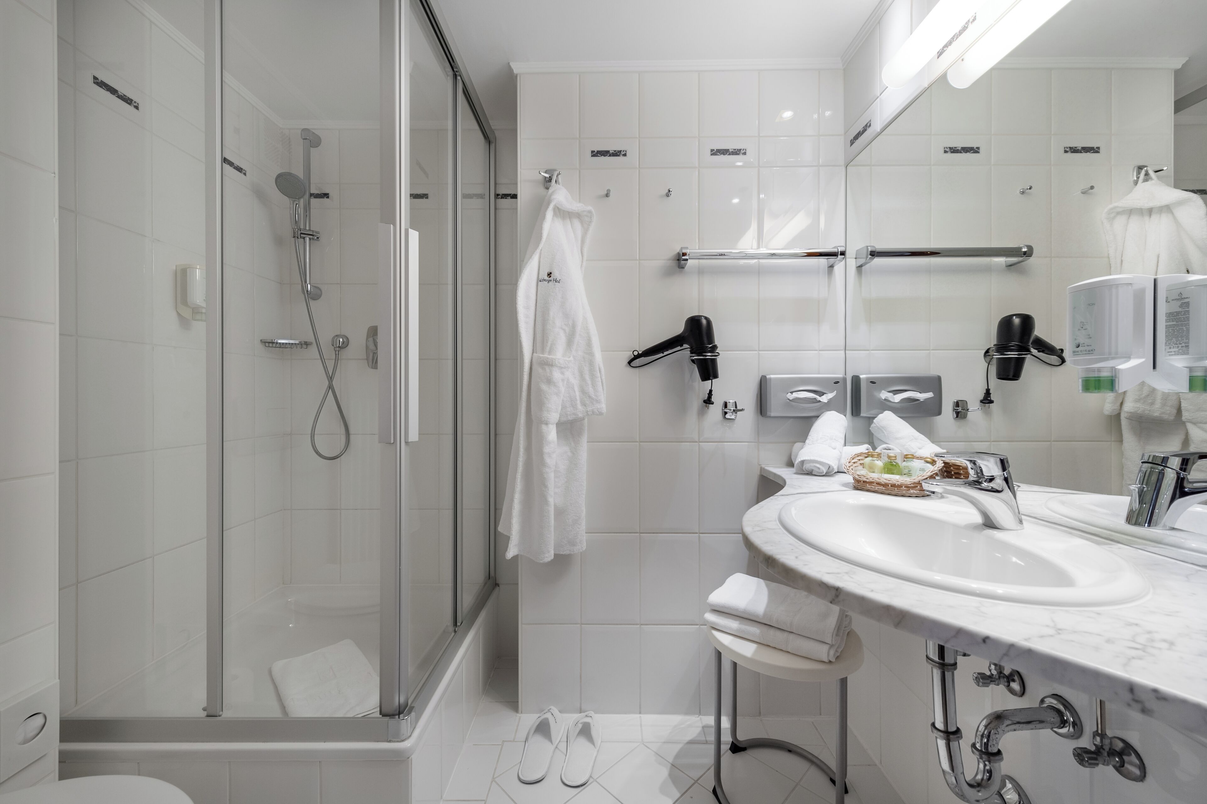 Un baño moderno con ducha envuelta en vidrio, un lavabo blanco con encimera de mármol y un espejo sobre el lavabo.