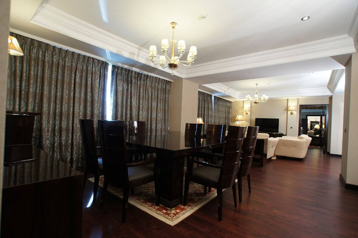 A dining area with a dark wooden table and chairs, a chandelier, and patterned curtains.