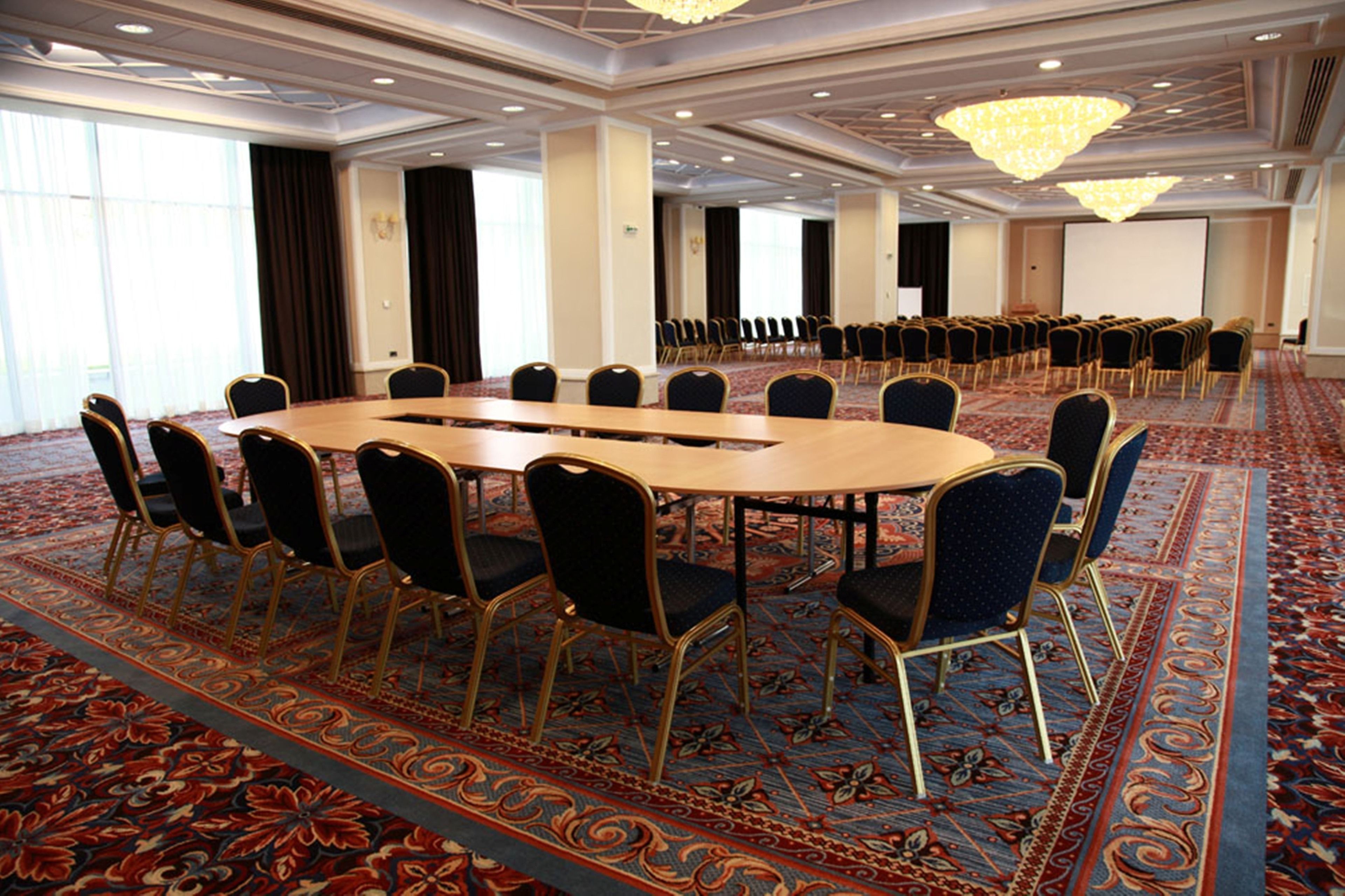 A conference room with a large oval table surrounded by chairs, carpeted flooring, and chandeliers.
