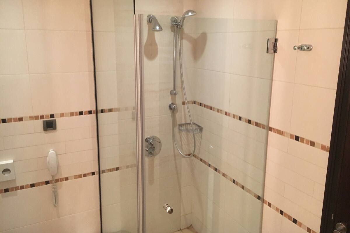 A glass-enclosed shower with a handheld showerhead and a wall-mounted faucet.