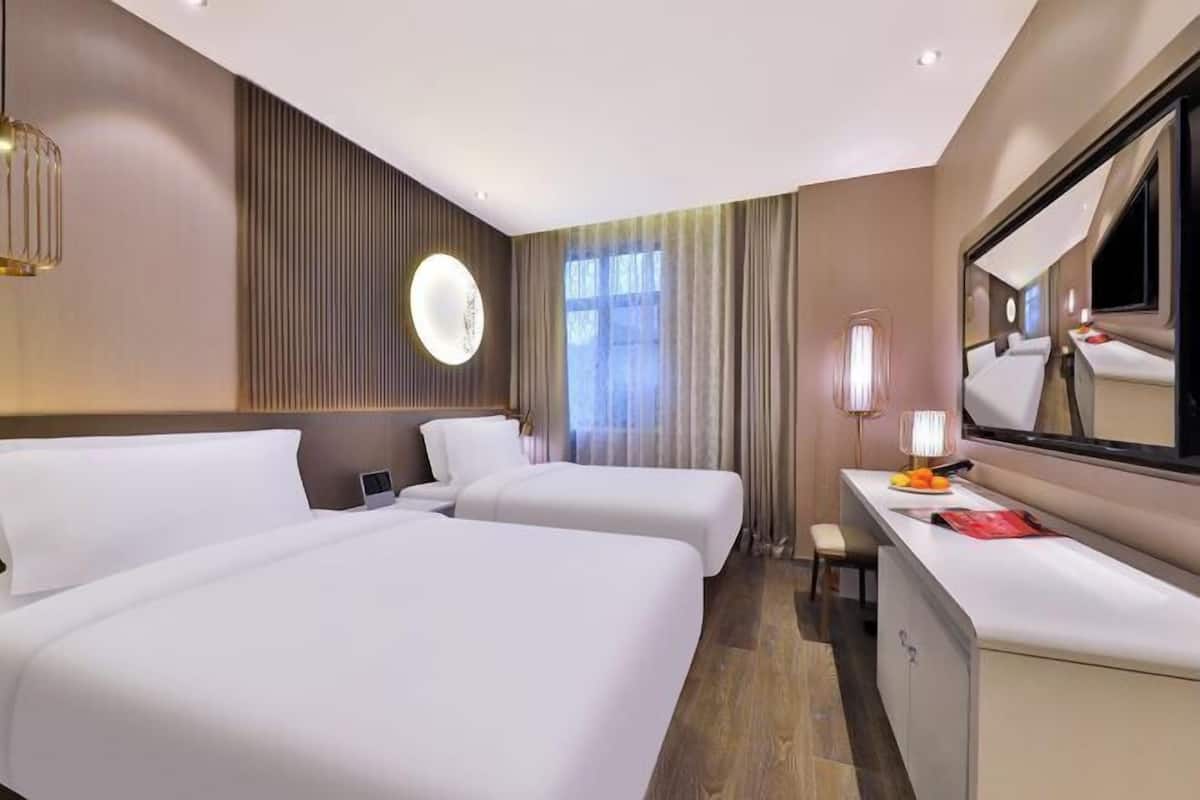 Habitación de hotel con dos camas, un escritorio, un espejo y una ventana con cortinas.