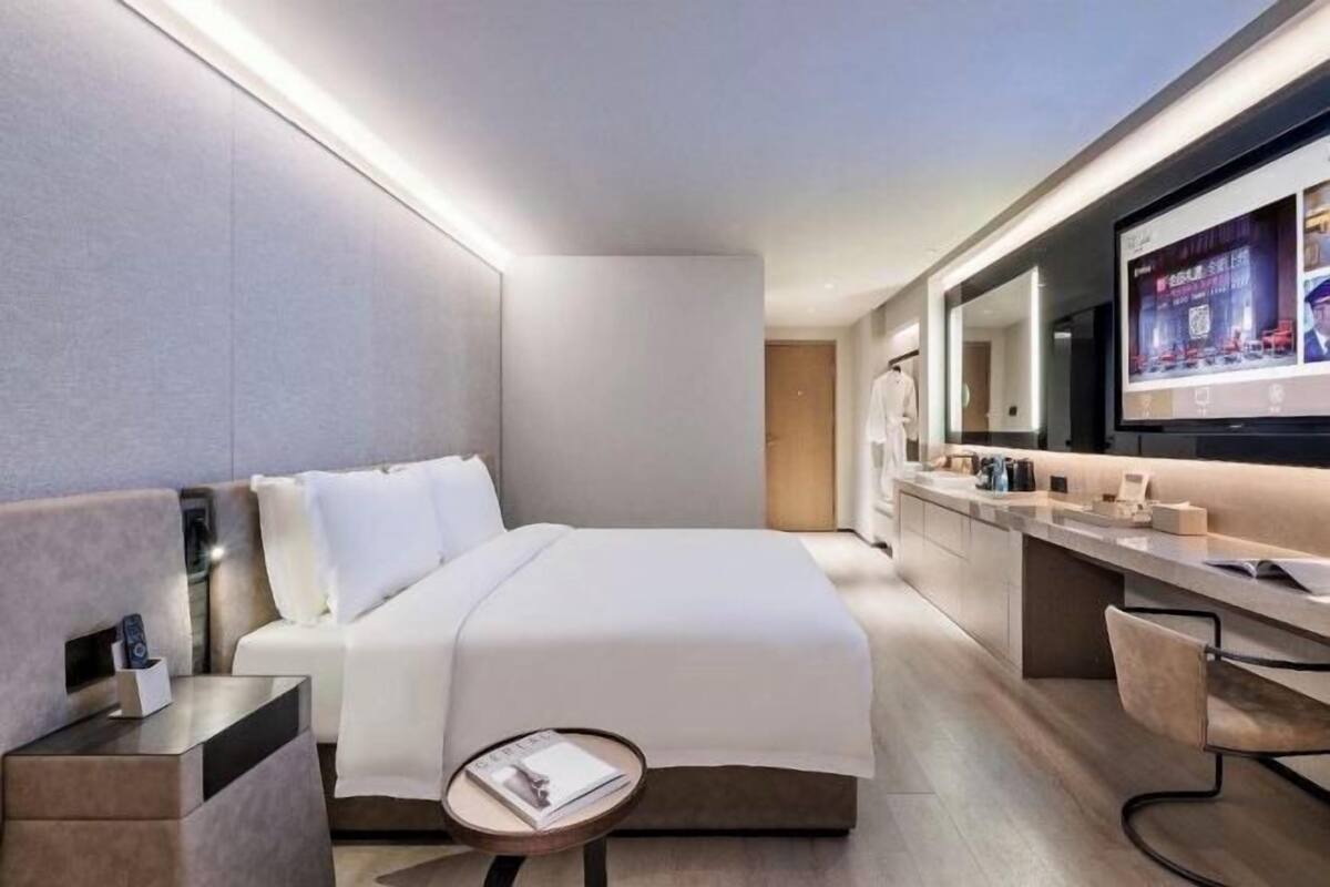 Una habitación de hotel moderna con una cama grande, una mesita de noche, una mesa redonda, un televisor y un minibar.