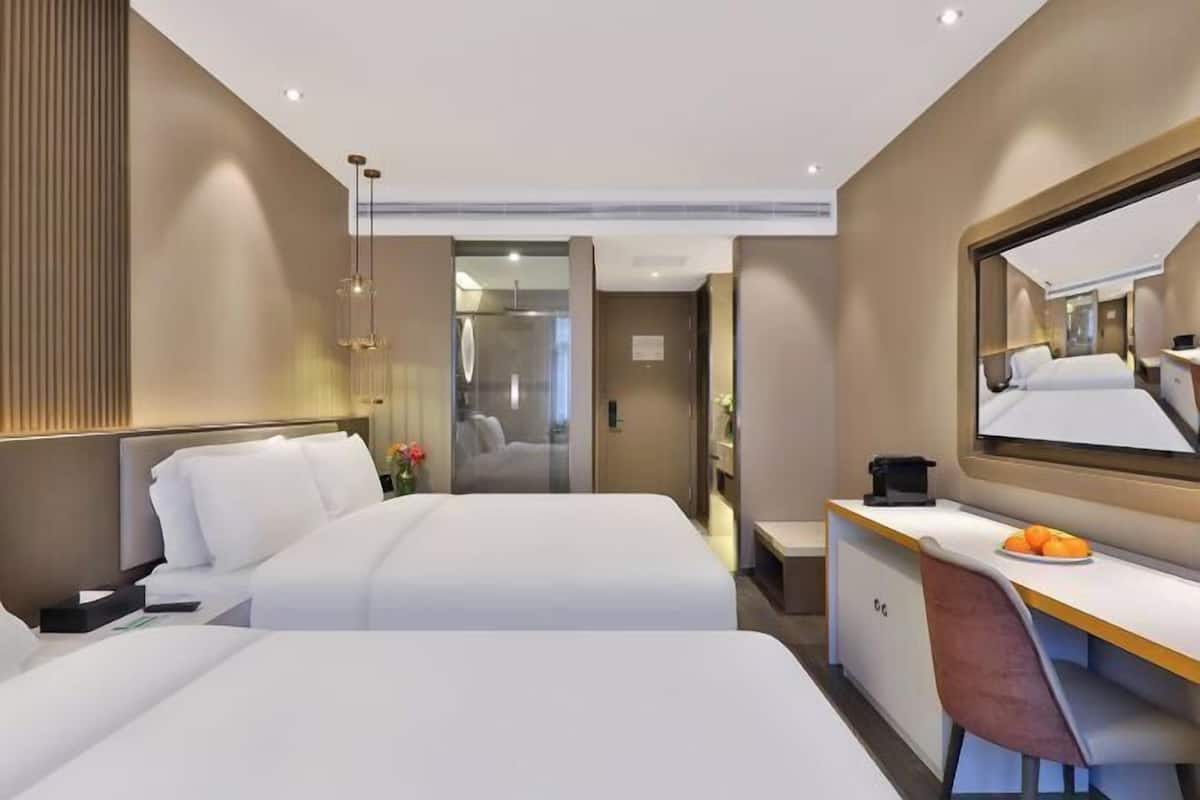 Una habitación de hotel moderna con dos camas, un escritorio y un espejo grande.