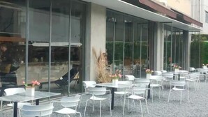An outdoor cafe with white tables and chairs, large glass windows, and a building facade in the background. - Orange Hotel Shanghai Longbai New Village Subway Station (Shanghai)