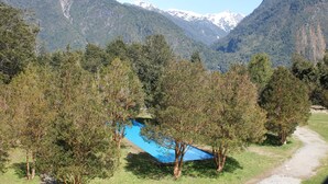 Paisaje montañoso con una piscina azul cristalina rodeada de árboles y un sendero que la lleva a ella.