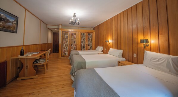 A hotel room with wooden paneling, two beds, a desk with a bottle and glasses, a chandelier, and a wall with patterned tiles. - Mitico Puelo Lodge (Cochamó)