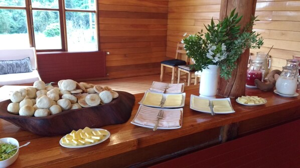A breakfast buffet with bread rolls, cheese, and butter on a wooden table. - Mitico Puelo Lodge (Cochamó)
