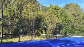 Una cancha de tenis con superficie azul, rodeada por una cerca de metal y árboles.
