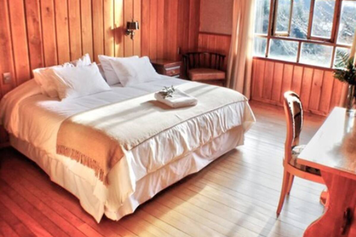 A wooden room with a bed, a chair, and a table.