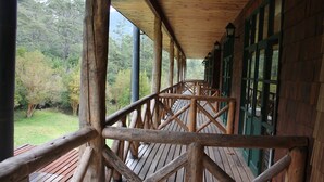 Una terraza de madera con barandillas, rodeada de árboles y un césped.